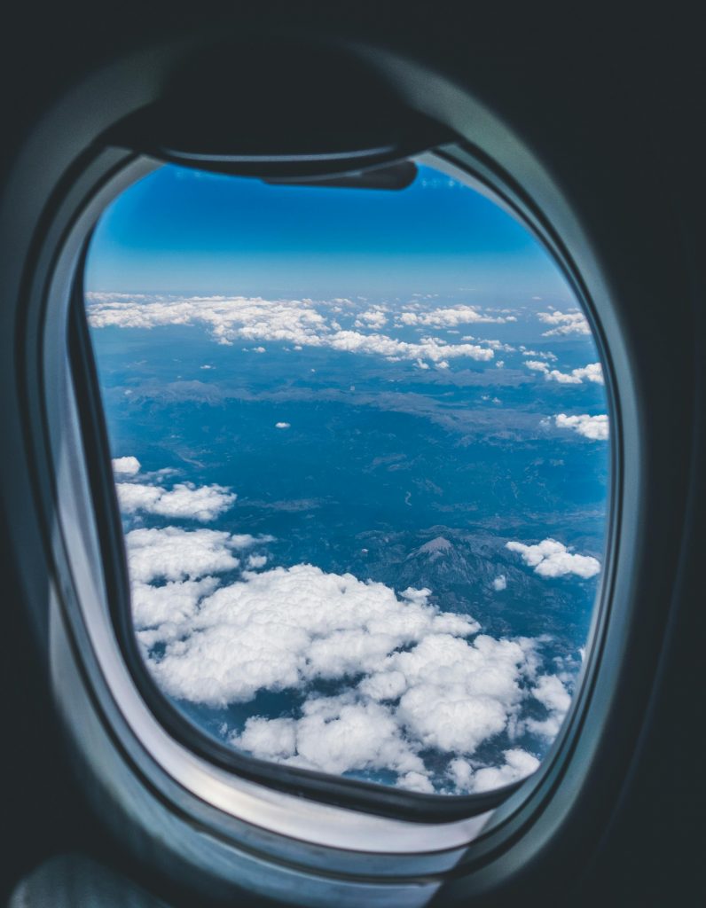 A stunning aerial view of clouds and landscape from an airplane window during a daytime flight.