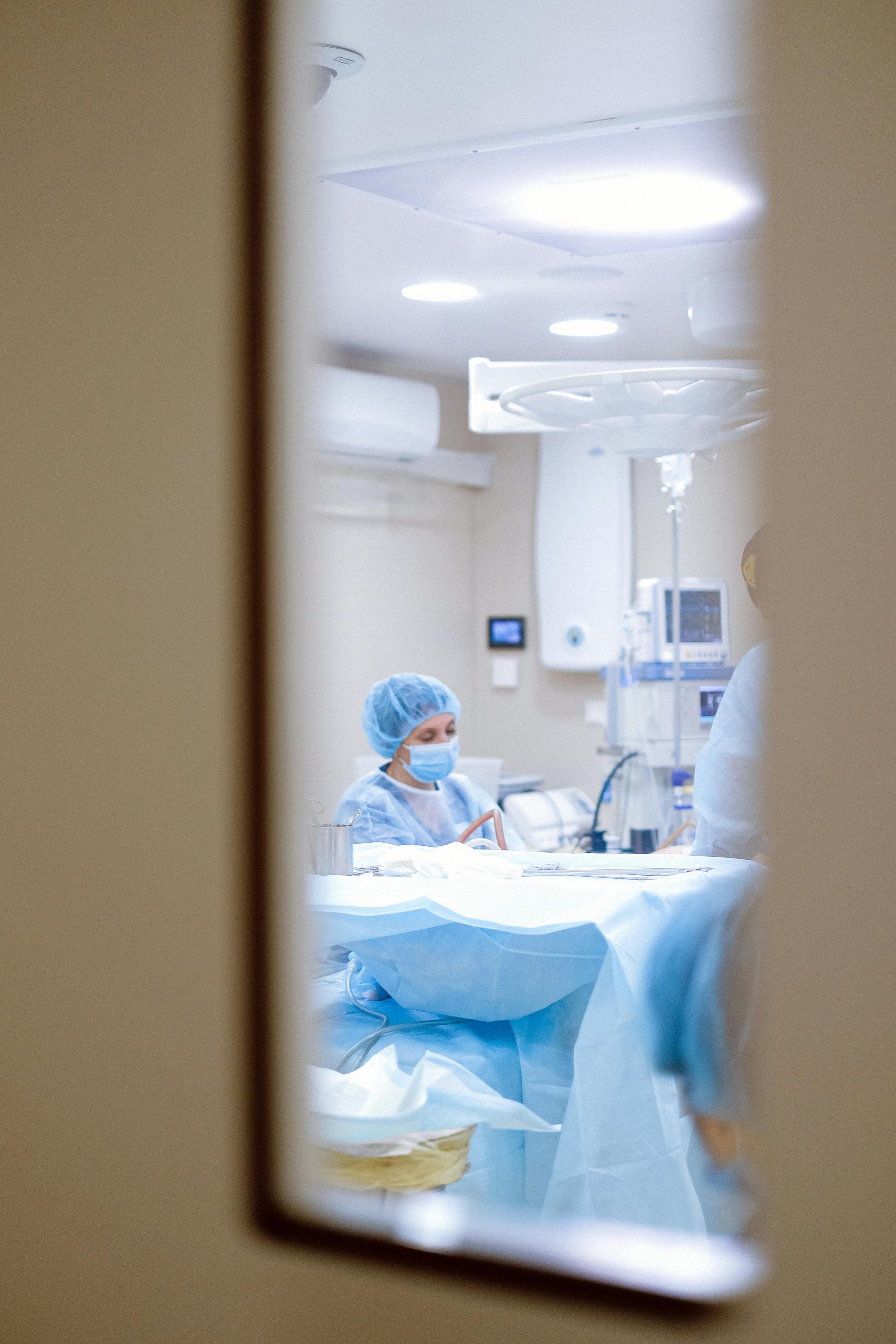 View of a surgeon working in an operating room through a door window, emphasizing medical precision.