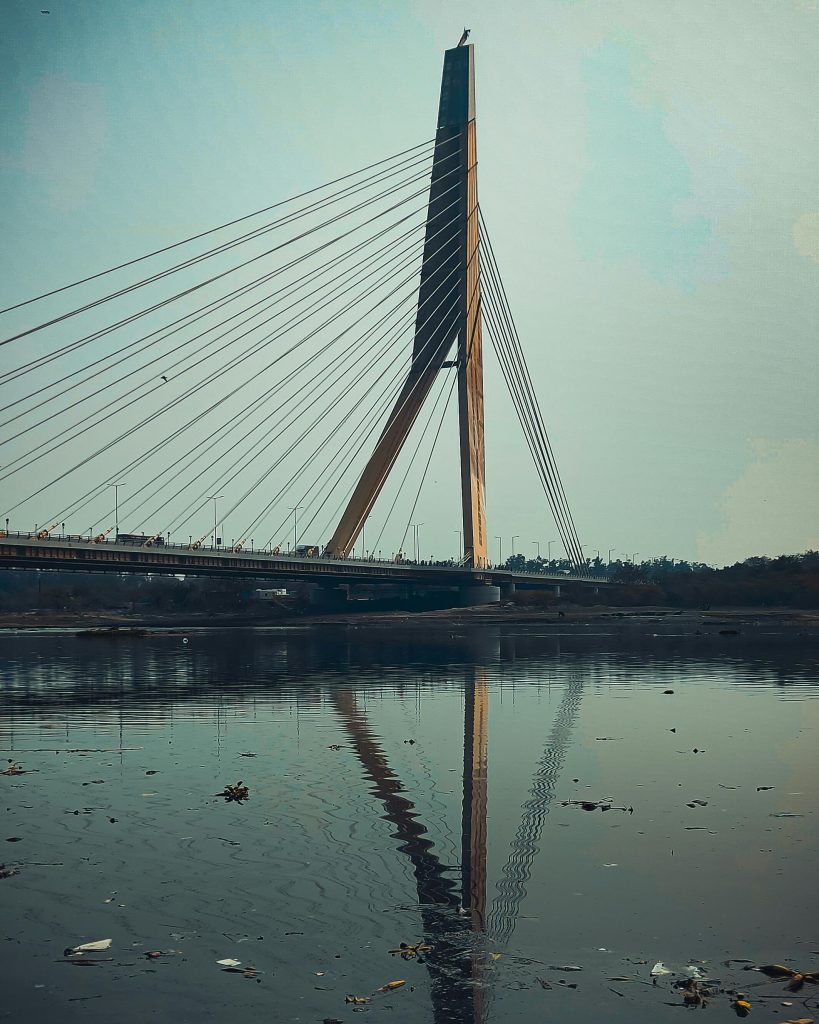Scenic view of a cable-stayed bridge over a river in Delhi with reflections on water.