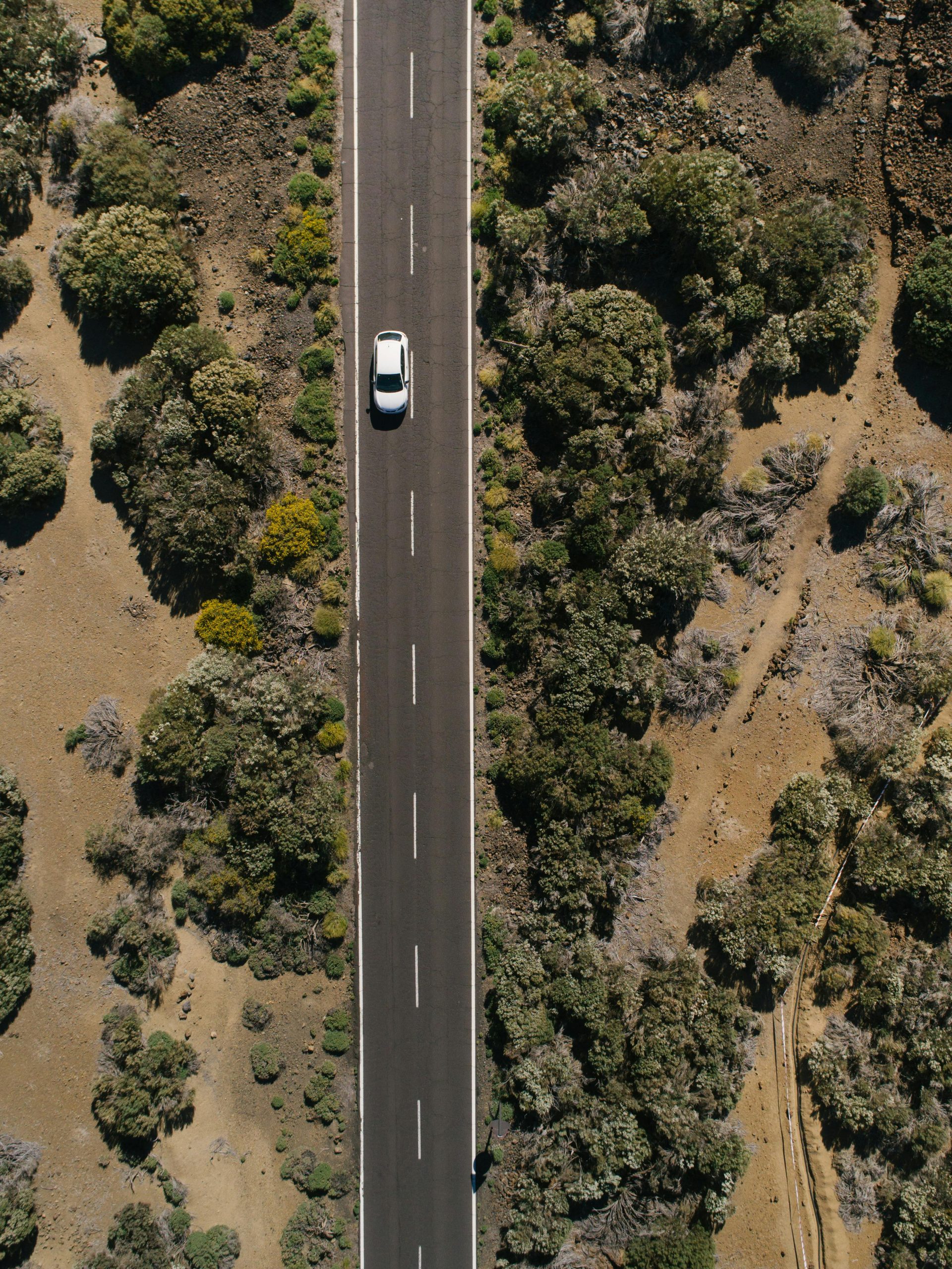 A scenic aerial shot capturing a lone car driving on a desert road surrounded by arid bushes.